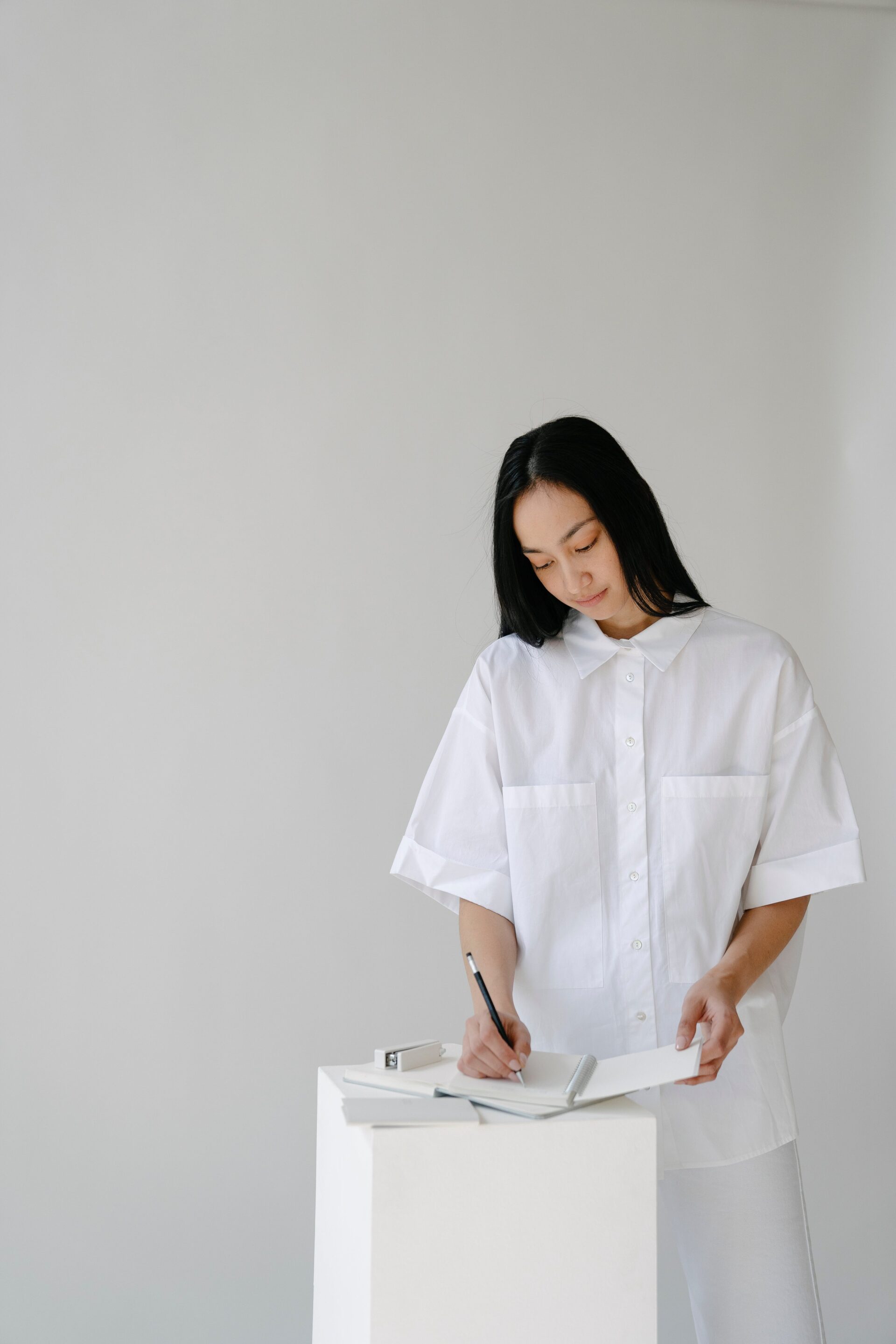 Focused nursing student in white attire writing notes on a pad, embodying dedication and the importance of detailed documentation in nursing education.