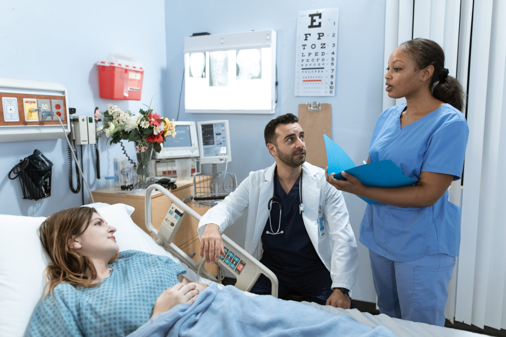 Doctor discussing patient's chart with nurse while patient listens in a hospital room