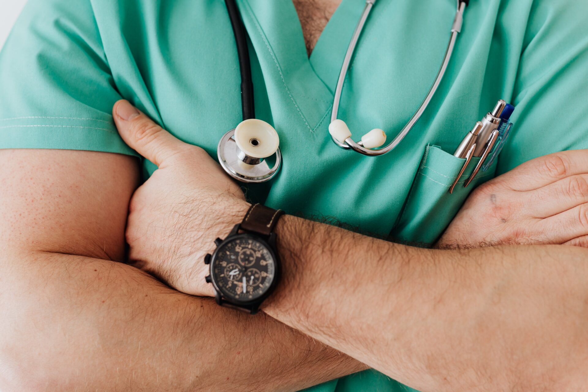 Close-up of a healthcare professional in teal scrubs with folded arms, showcasing a stethoscope, pens in pocket, and a wristwatch, representing readiness and professionalism in nursing practicum.