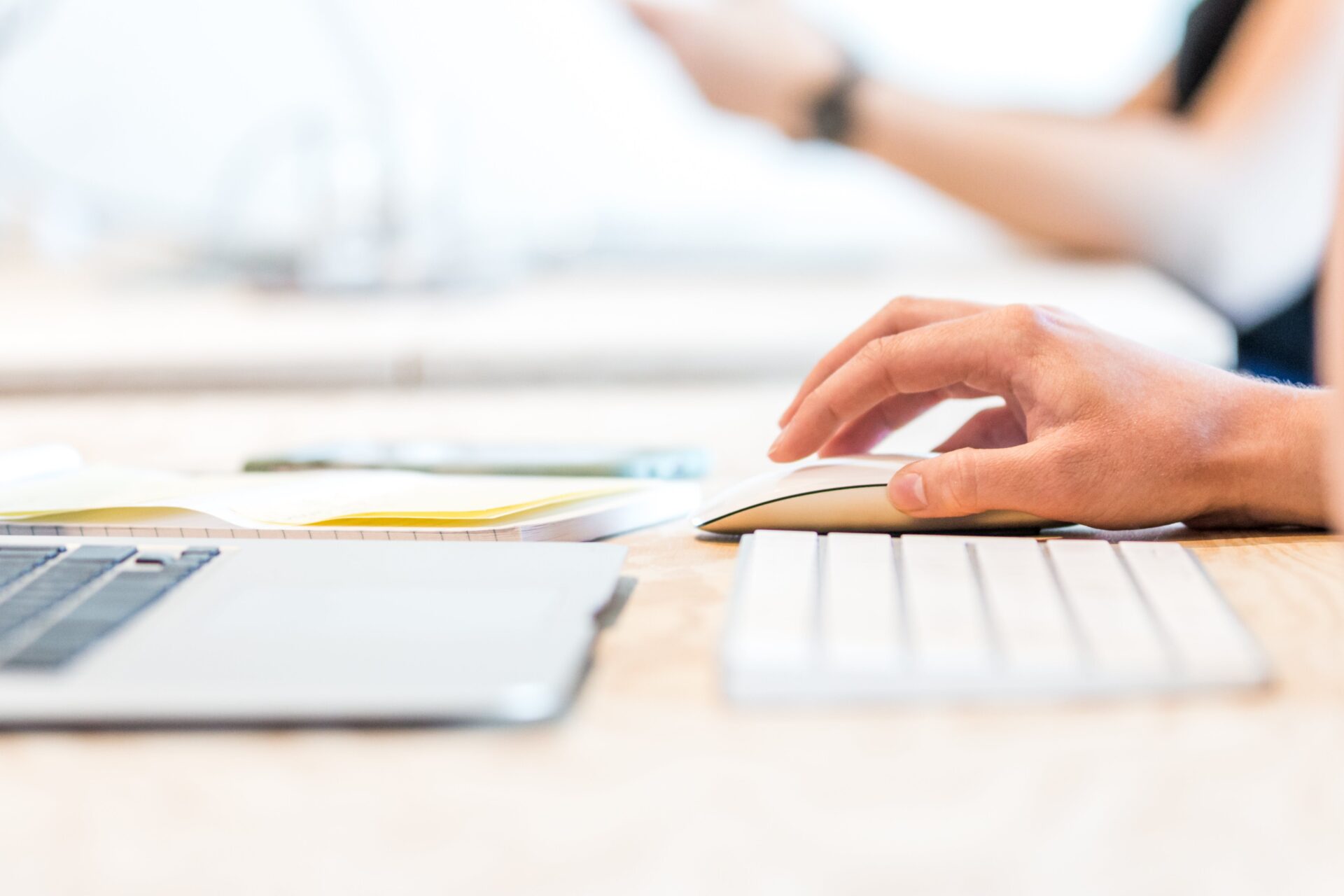 Close-up of a student's hand using a mouse while working on a nursing essay with notes and a laptop on the desk.