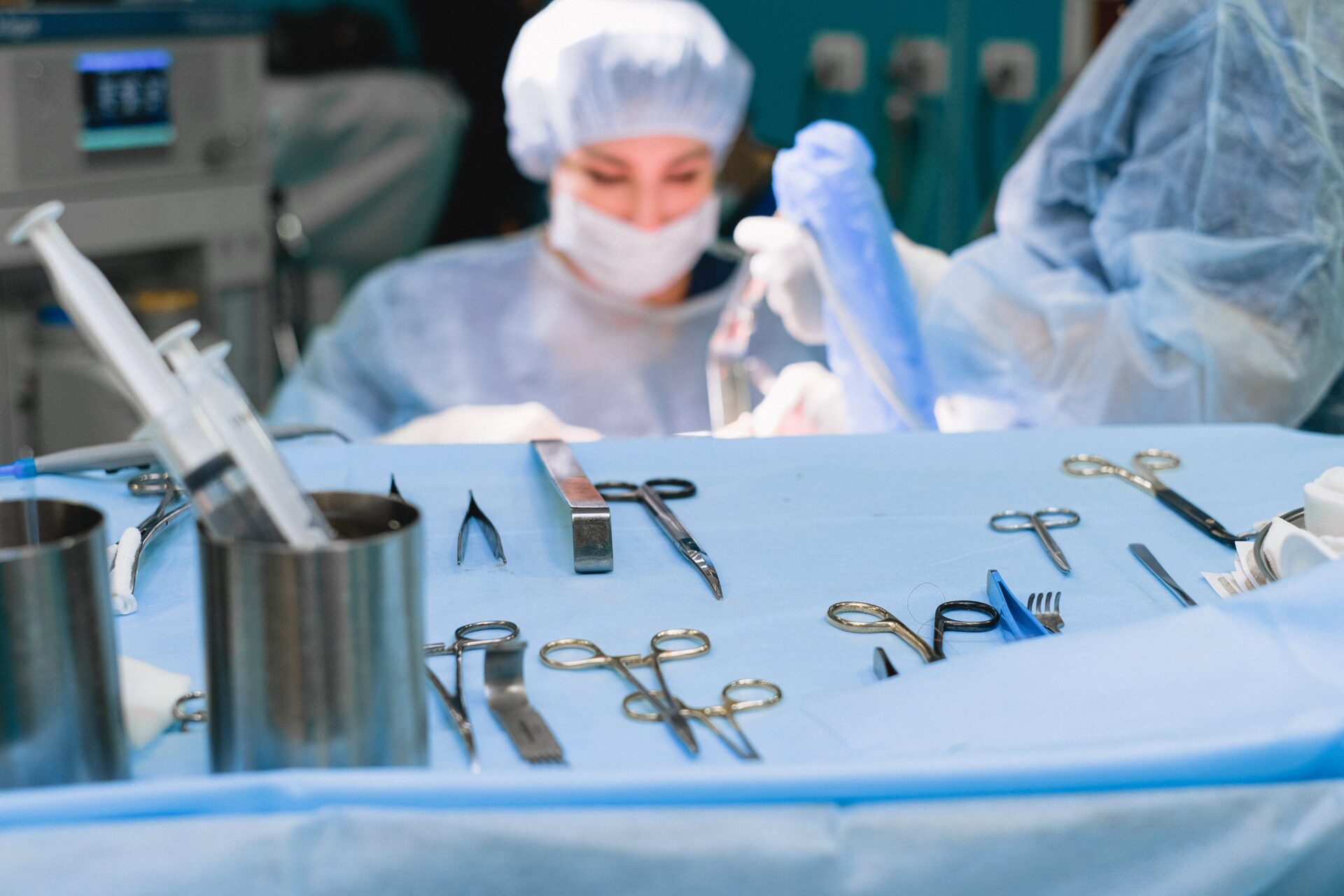 Surgical instruments laid out on a sterile blue drape with a nurse preparing equipment in the background