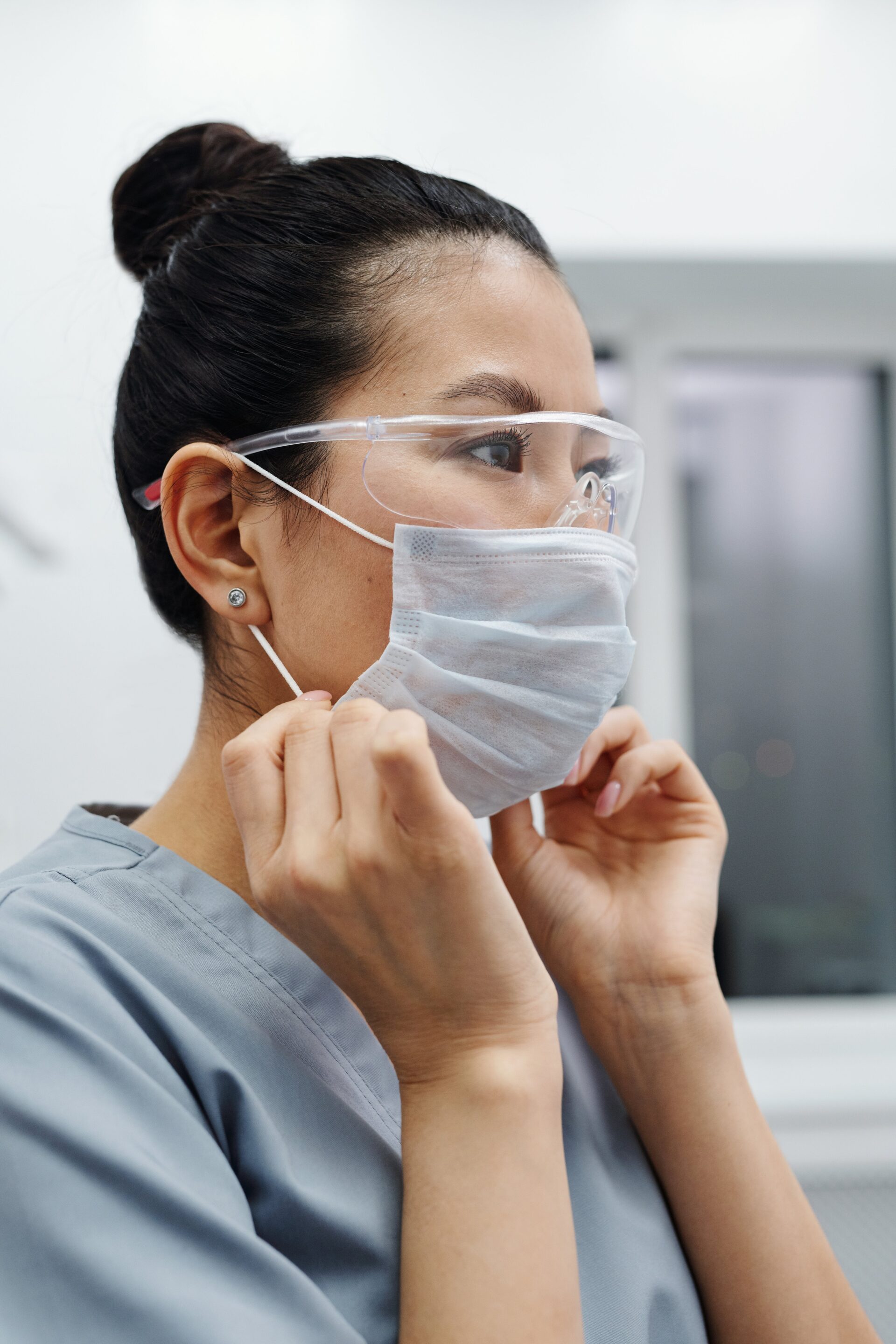 Healthcare professional diligently putting on a protective face mask and safety goggles to ensure safety and hygiene in a clinical setting.