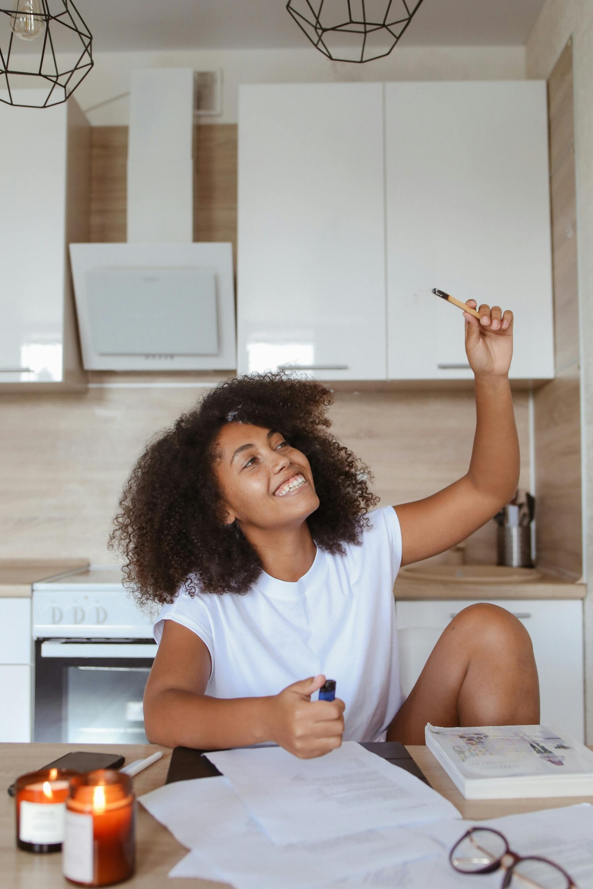 A cheerful nursing student finding inspiration while studying with notes and books on a kitchen table, with a lit candle adding a cozy atmosphere to her study session.