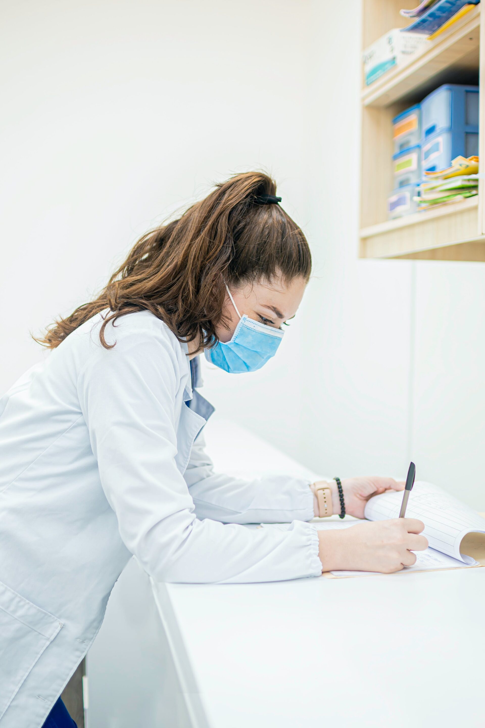 Close-up of a person's hands writing an essay with notes and textbooks around, symbolizing the process of crafting a winning nursing program application essay.