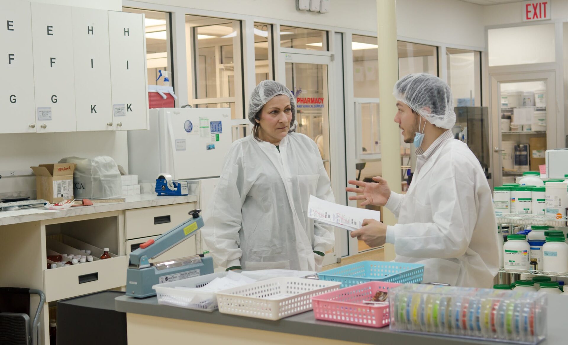 Two healthcare professionals in lab coats discussing medication protocols in a hospital pharmacy