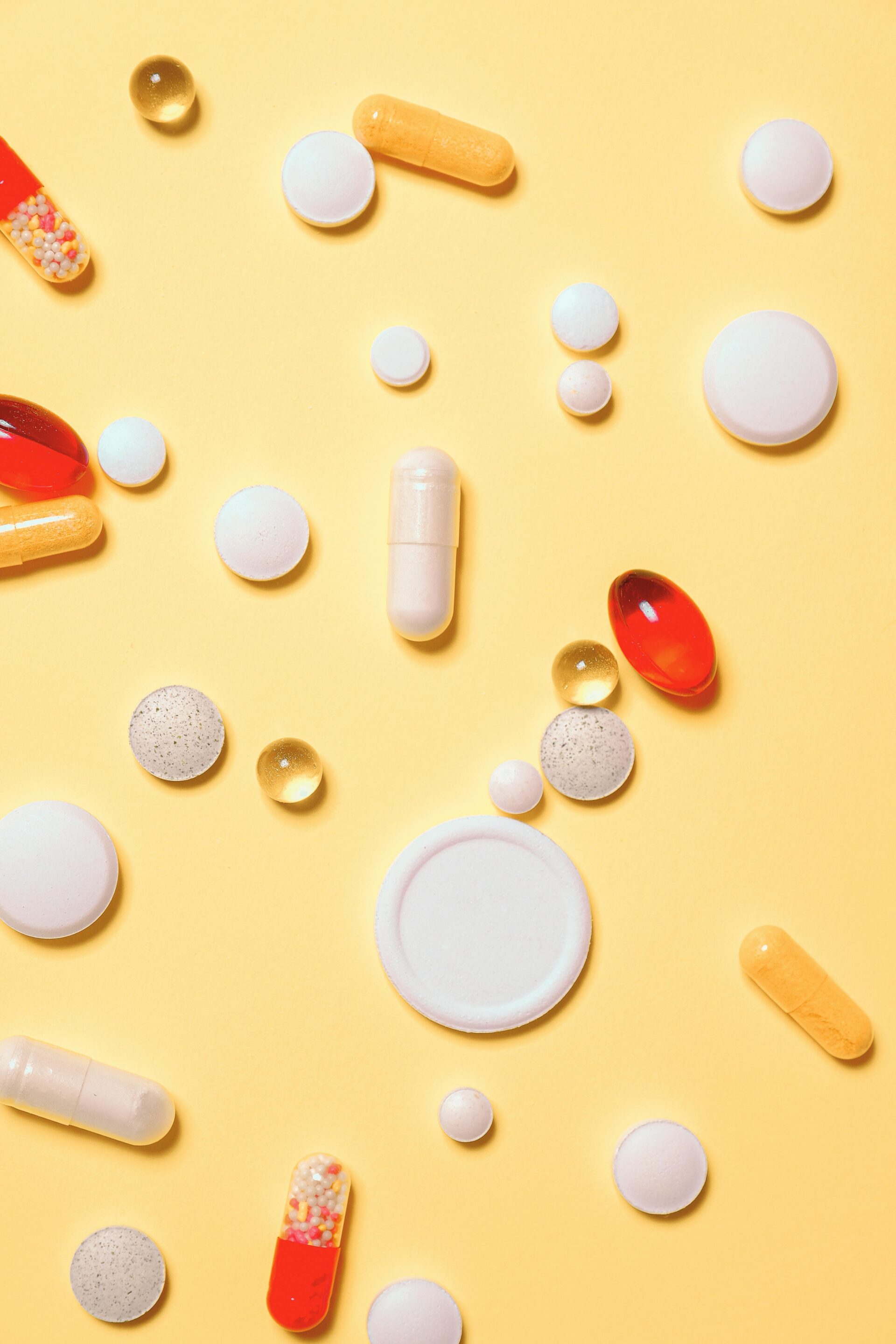 Assorted prescription pills and capsules scattered on a yellow background, illustrating diverse pharmaceutical medications.