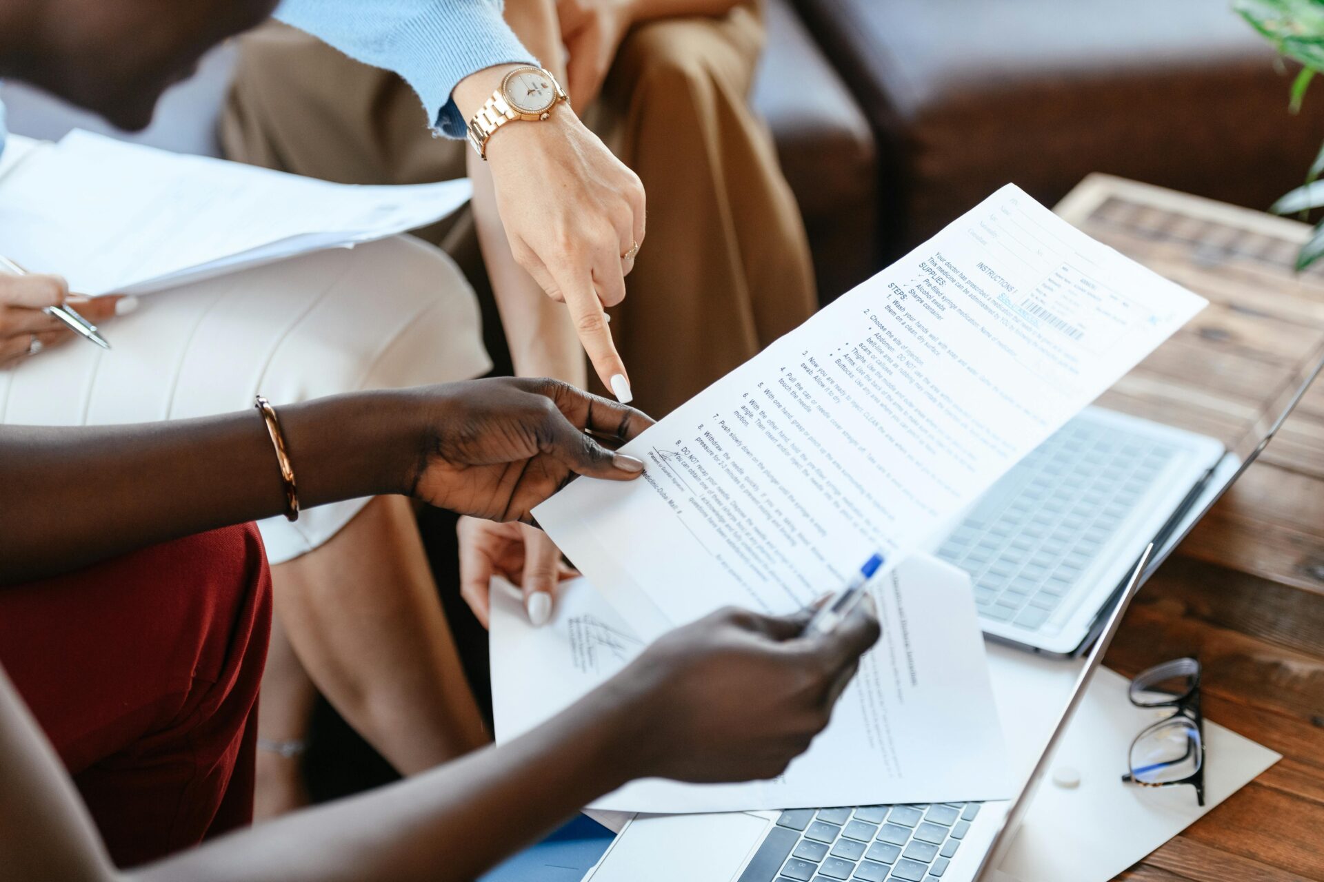 Close-up of a diverse team of professionals reviewing a nursing research paper, with one person pointing to a section of the nursing research paper.