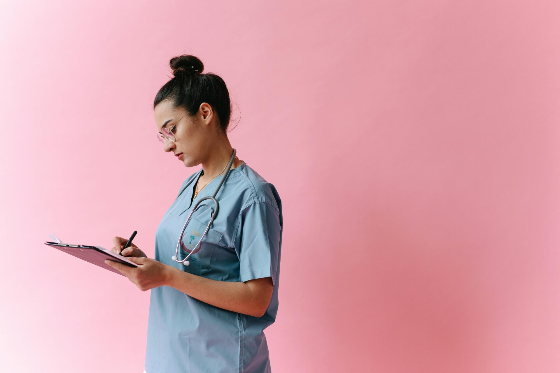 A nurse demonstrating how to write nursing notes on a clipboard with a stethoscope around her neck