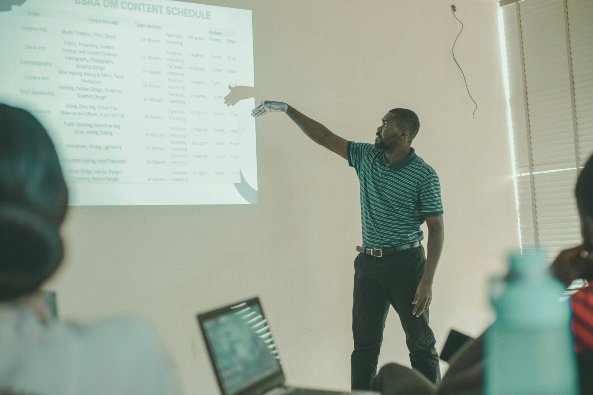 A man presenting a content schedule on a projector screen to a group, relevant to creating a Nursing PowerPoint presentation.